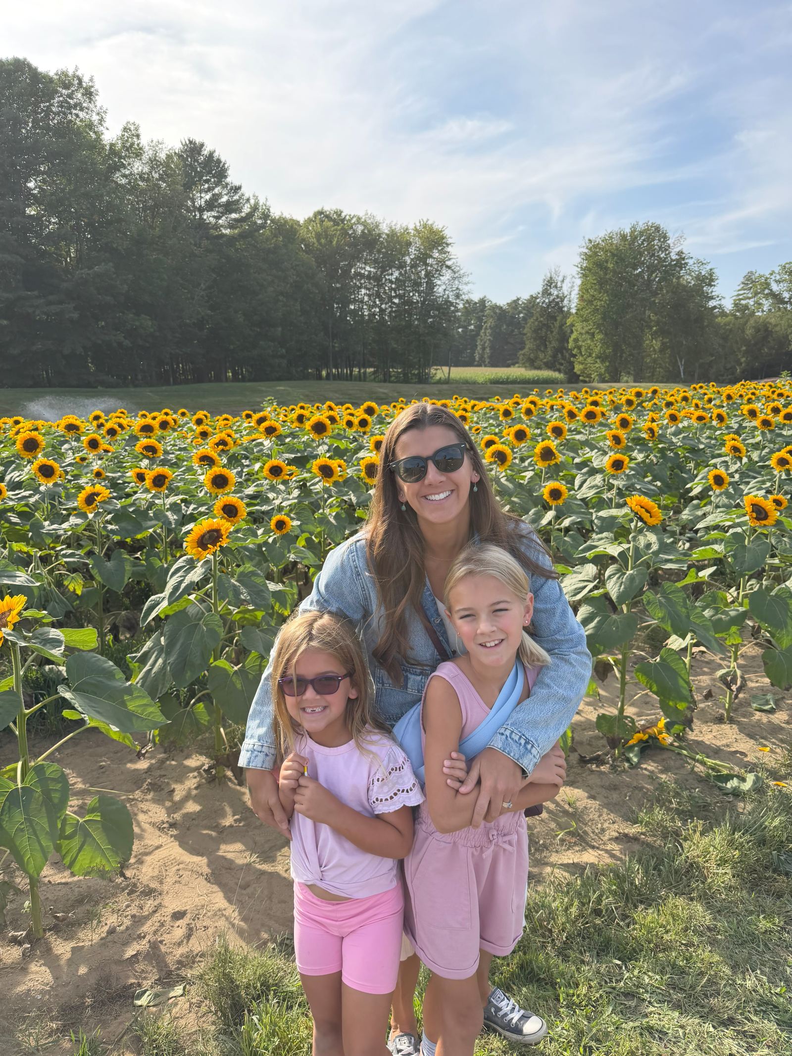 Kailah and her daughters smiling in a Massachusetts sunflower field in early fall