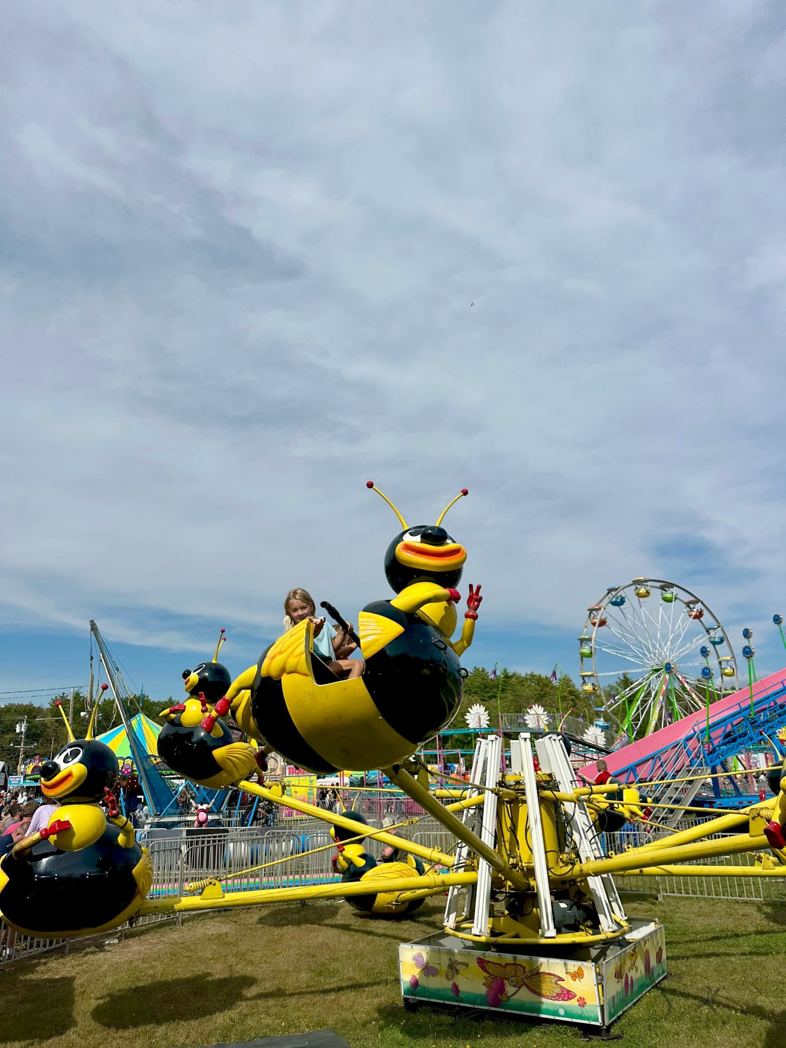 A girl riding the bee ride at Topsfield Fair with the Ferris wheel behind her